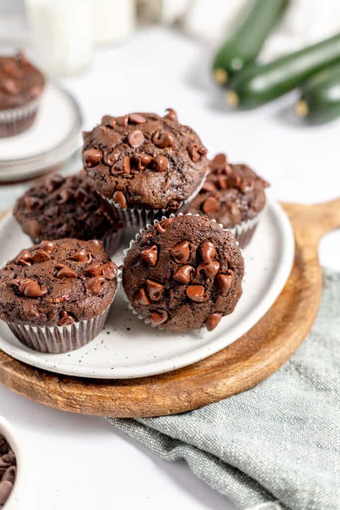 A pile of chocolate zucchini muffins on a white plate on a cutting board. 