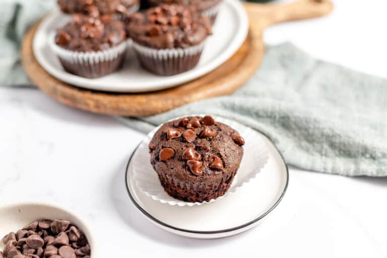 Double chocolate zucchini muffin in a plate with the rest of the muffin in the background.
