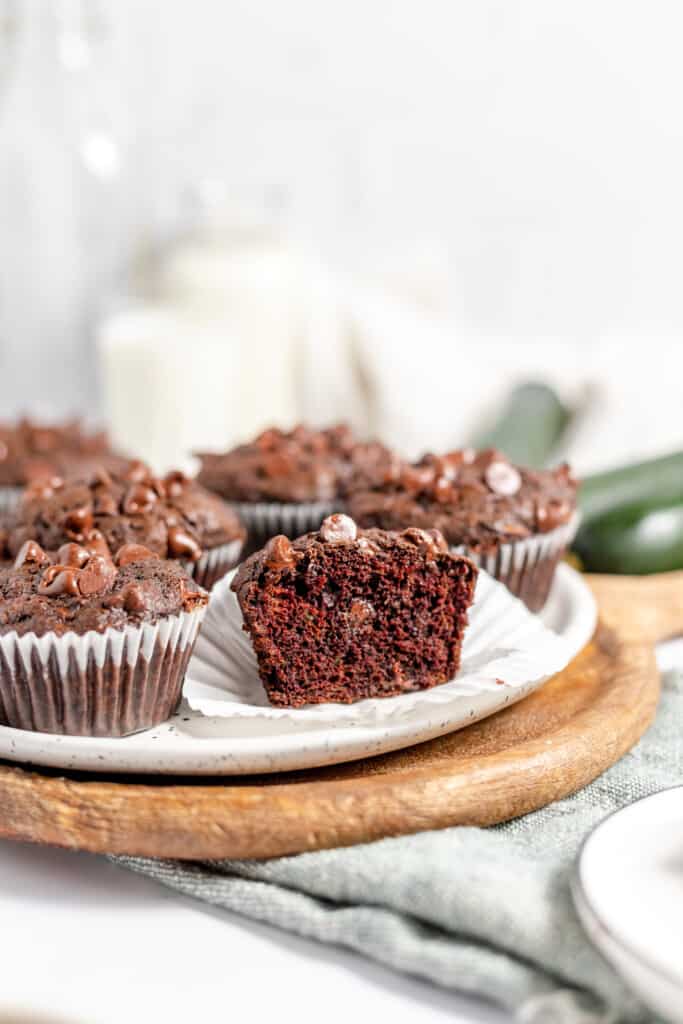 Half a chocolate zucchini muffin on a white plate with other muffins around it. 