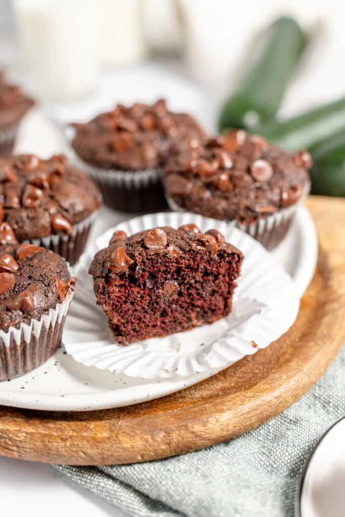Chocolate zucchini muffins with chocolate chips, one split open to show the moist interior, on a wooden board.
