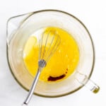 Eggs, sugar, vanilla extract in a bowl with a whisk.