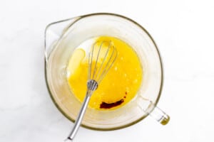 Eggs, sugar, vanilla extract in a bowl with a whisk.