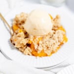Peach crumble on a white plate with ice cream and a fork.