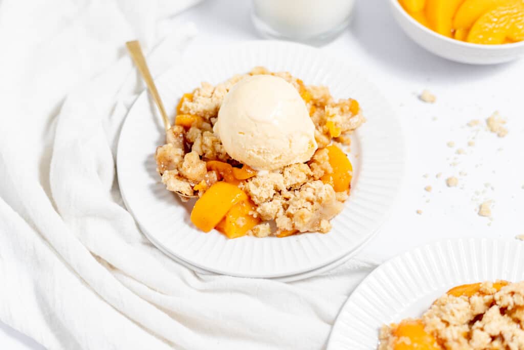 Close-up photo of peach crumble topped with vanilla ice cream.
