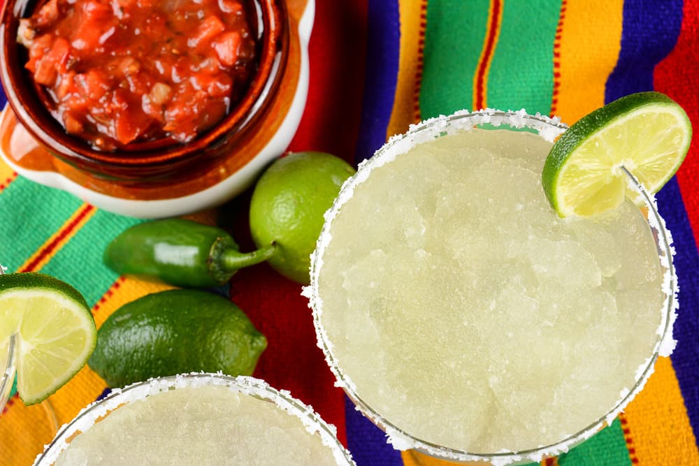 Margaritas with limes and a bowl of salsa.