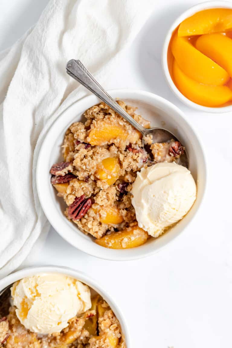 A bowl of peach crisp served with vanilla ice cream with the rest of peach on the side.