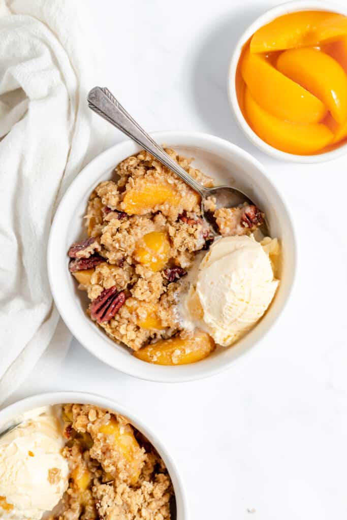 Two bowls of peach crisp with vanilla ice cream.