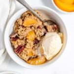 A big bowl of peach crisp with a spoon and vanilla ice cream.