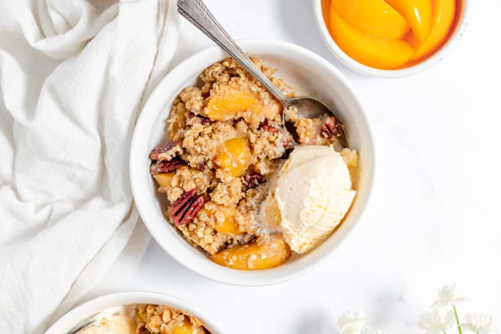 Peach crisp with vanilla ice cream with a spoon..