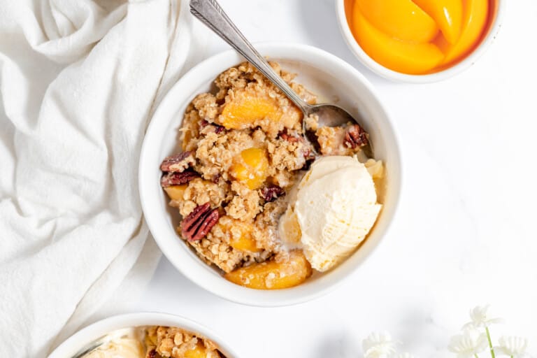 Peach crisp with vanilla ice cream with a spoon..