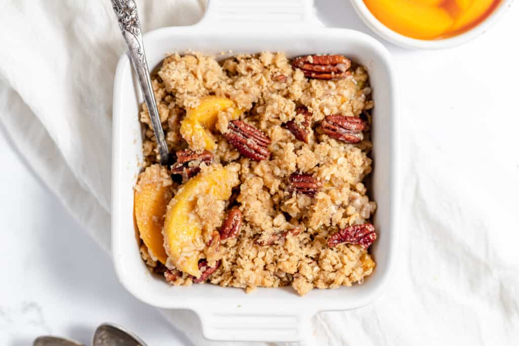 A pan full of peach crisp with a spoon ready to scoop.