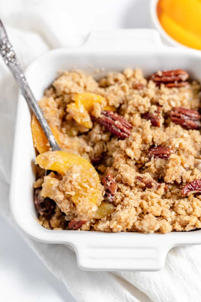 Scoop of peach crisp being lifted out of the baking dish.