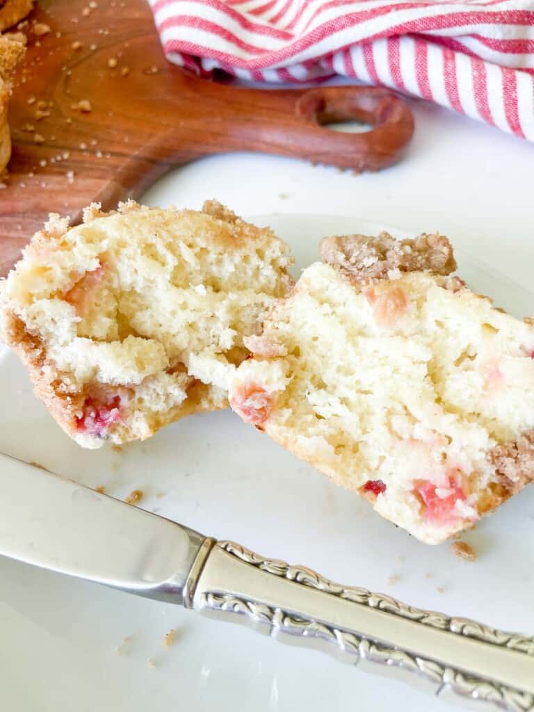 A split rhubarb muffin on a plate with a knife. 
