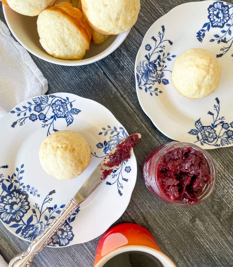 Lemon muffins on plates with a bowl of muffins, and jelly. 