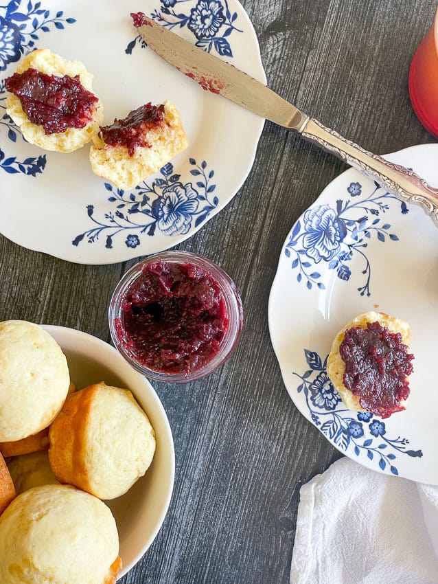 Lemon muffins slathered with raspberry jam, a bowl of muffins, and a knife. 