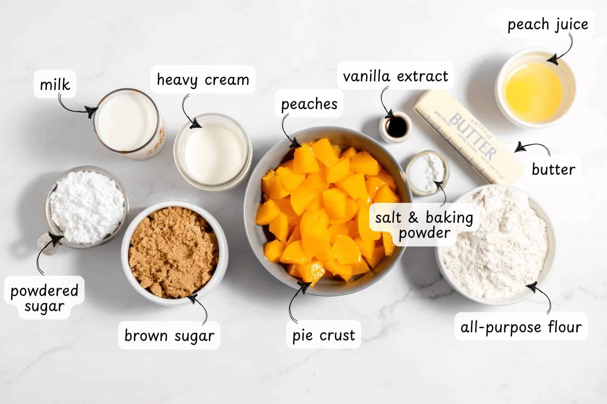Ingredients for a delightful peach cake on a marble surface: milk, heavy cream, vanilla extract, butter, peach juice, peaches, pie crust, all-purpose flour, salt and baking powder, brown sugar, and powdered sugar.