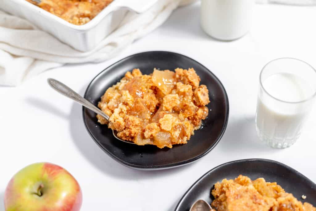 A plate of apple crisp with a spoon and a glass of milk.
