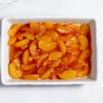 Sliced peaches in a white dish on a marble countertop.