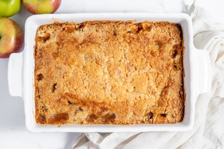Apple crisp in a white dish with apples next to it.