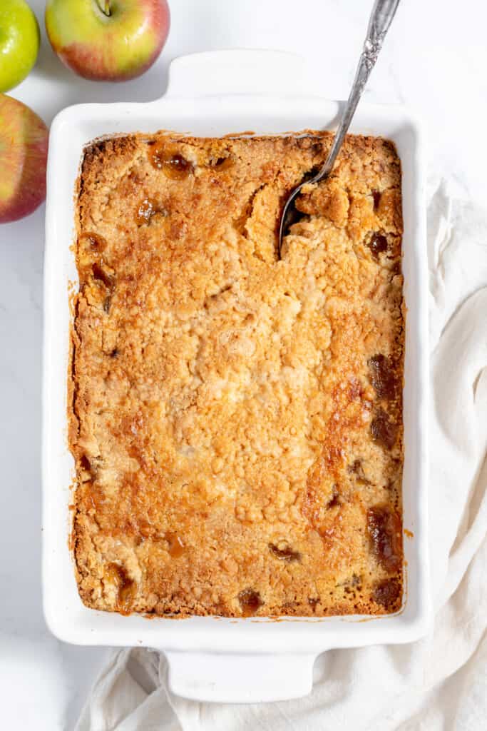 Apple crisp in a white baking dish with a spoon.