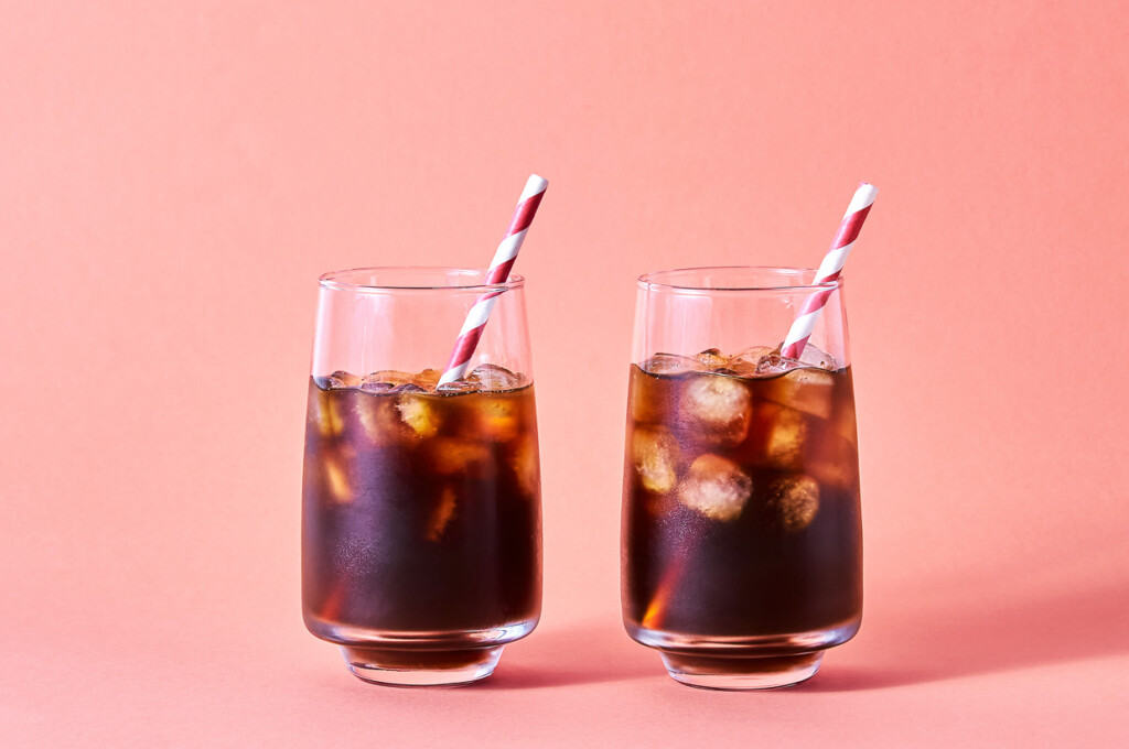 Two glasses of iced coffee on a pink background.