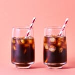 Two glasses of iced coffee on a pink background.