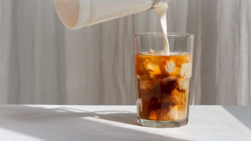 An iced coffee being poured into a glass.