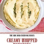 A white dish filled with fluffy whipped potatoes, garnished with sprigs of thyme, sits on a red and white striped towel.
