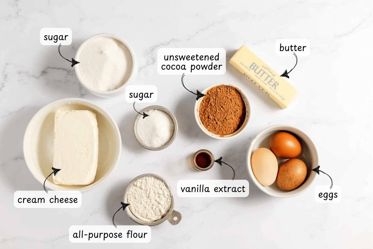 On a marble surface, gather the essentials for baking: cream cheese, all-purpose flour, sugar, unsweetened cocoa powder, vanilla extract, eggs, and a stick of butter. Perfect ingredients for creating delicious cheesecake brownies.