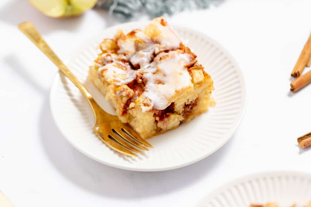 A slice of apple cinnamon roll cake on a plate with a gold fork.