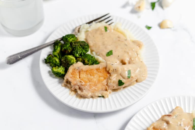 A plate of creamy garlic chicken served with mashed potato and broccoli.