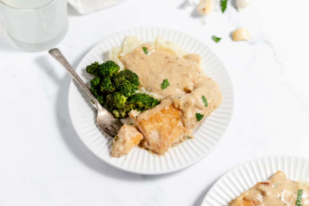A bite of chicken on a fork on a white plate with garlic sauce over mashed potatoes.