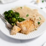A bite of chicken on a fork on a white plate with garlic sauce over mashed potatoes.