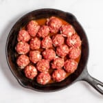 Enchilada meatballs cooked in a skillet on a marble countertop.