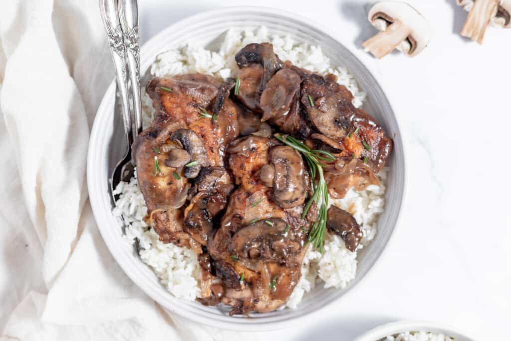 Mushrooms and rice in a white bowl topped with chicken marsala sauce.
