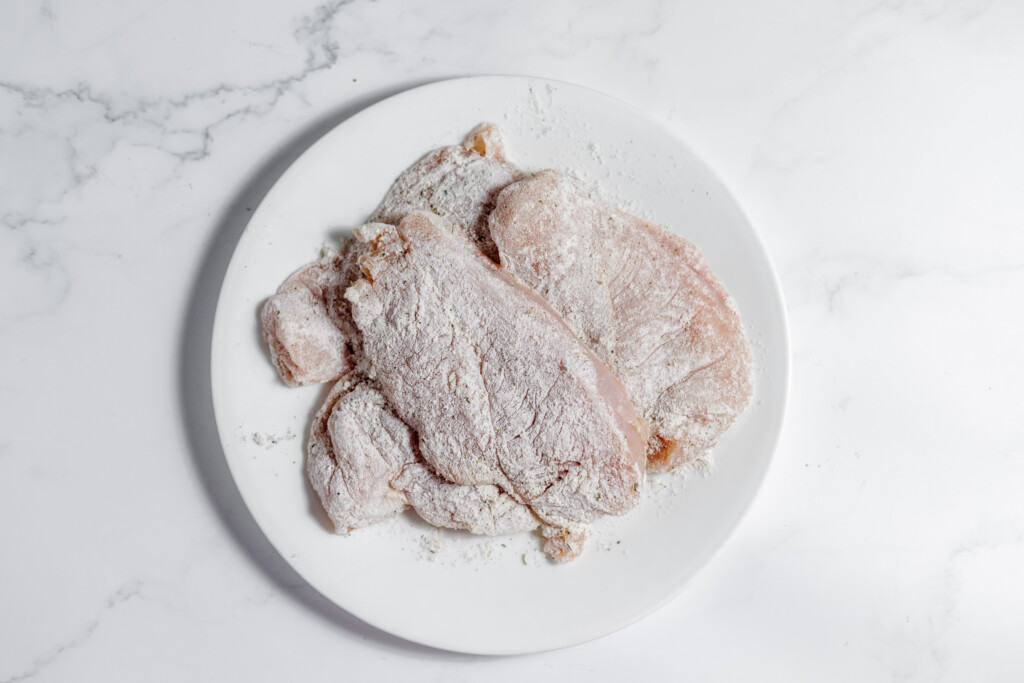 Frozen chicken breasts on a white plate ready to be transformed into a delicious chicken marsala dish.