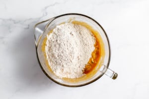 A glass bowl with pumpkin and zucchini bread ingredients.