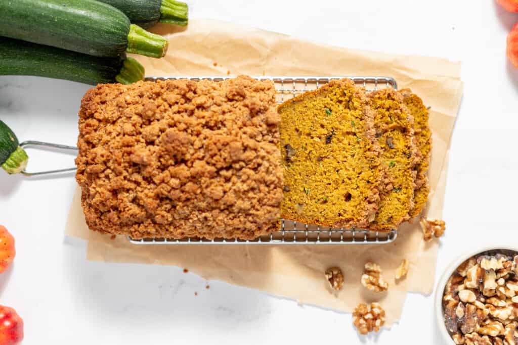 A loaf of pumpkin zucchini bread is sitting on a cooling rack.