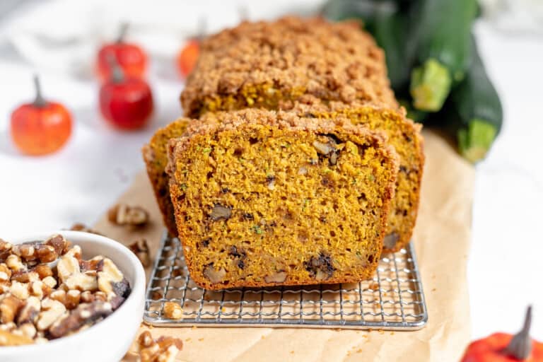 A loaf of pumpkin zucchini bread with walnuts on a cooling rack.