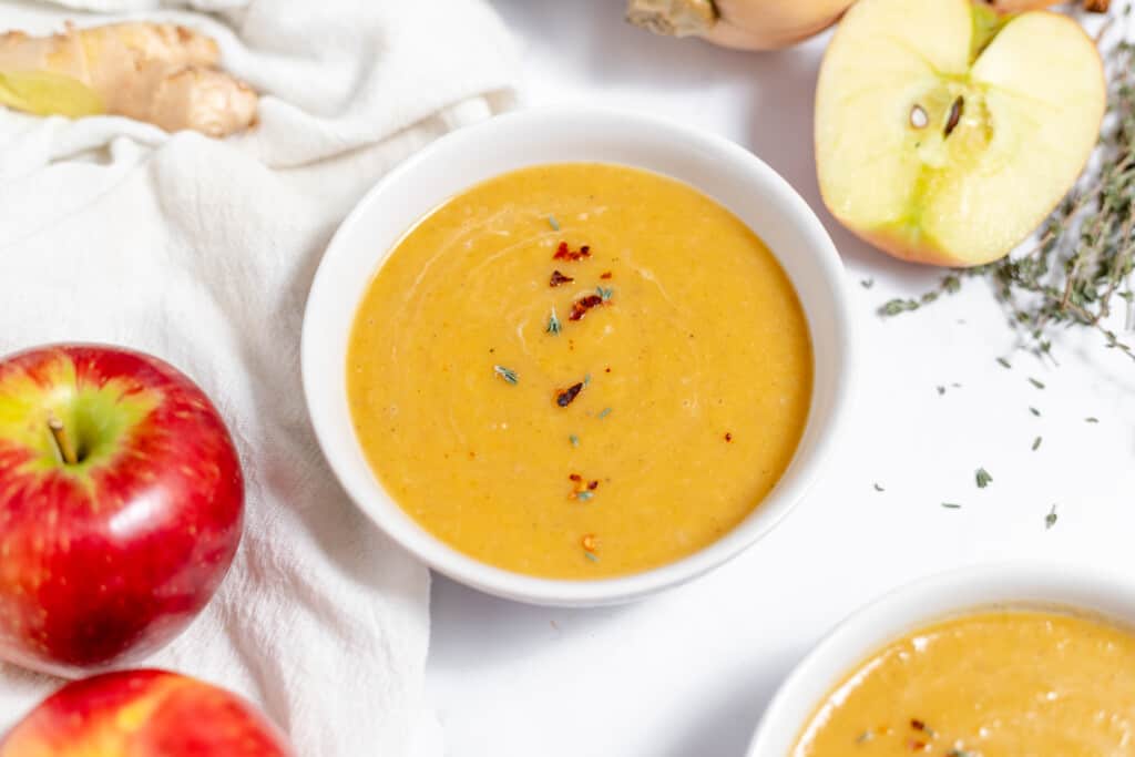 A bowl of soup with apples and herbs.
