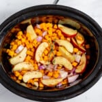 A crock pot filled with apples and onions.