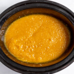A crock pot filled with carrot soup.
