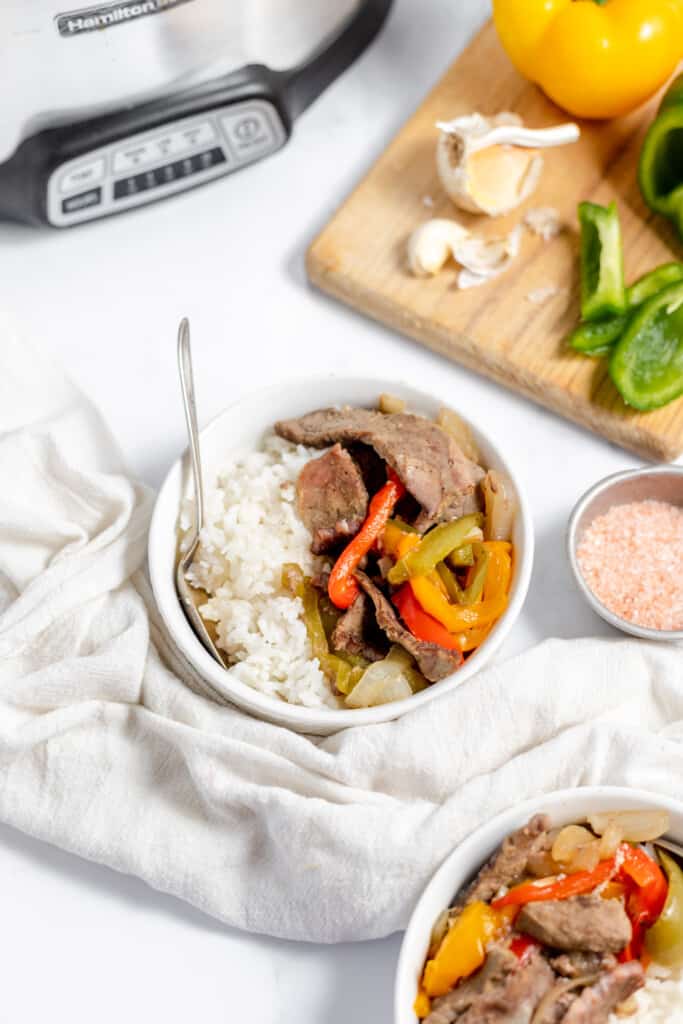 A bowl of rice with beef and peppers in front of an instant pot.
