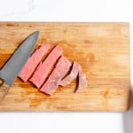 Sliced beef on a cutting board next to a knife.