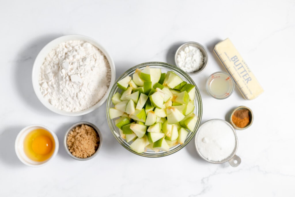 Apple pie ingredients on a white marble table.