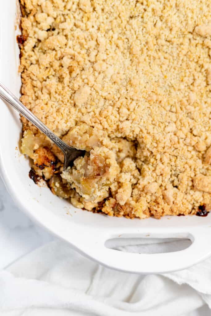 An apple crumble casserole with a spoon in a white dish.