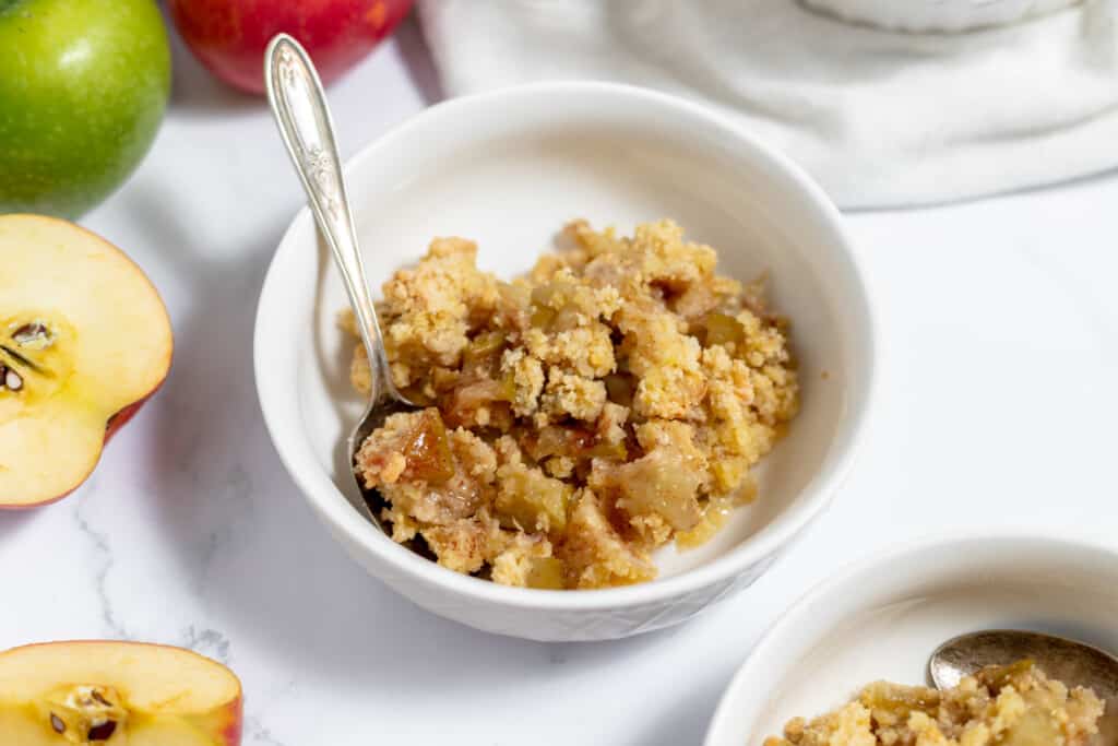 Two bowls of apple crumble with spoons next to them.