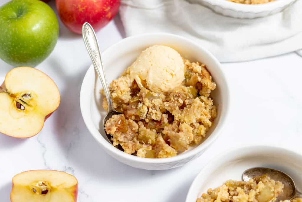 A bowl of apple crisp with ice cream and apples.