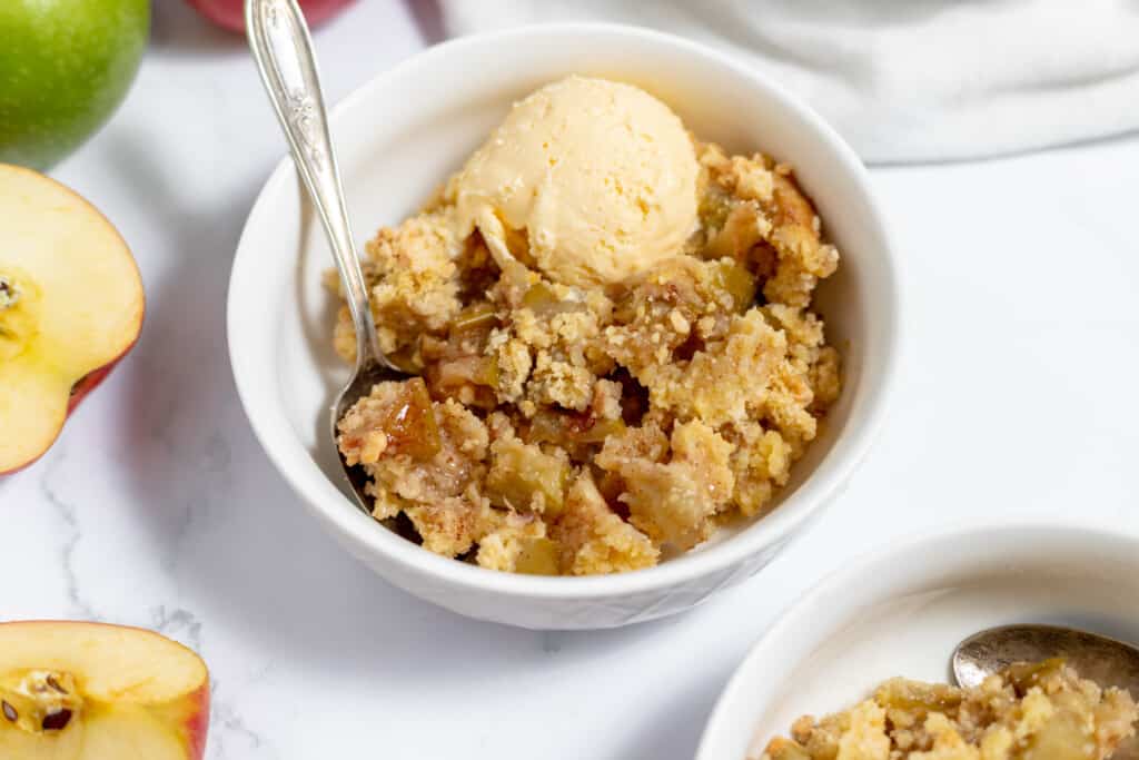 A bowl of apple crisp with ice cream and apples.