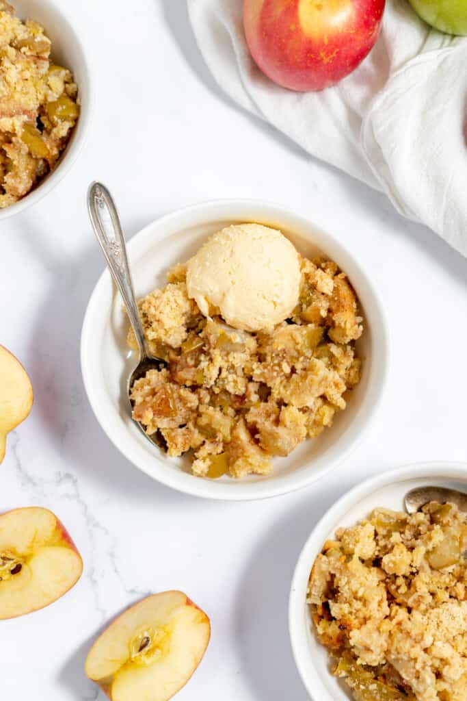 Three bowls of apple crisp with ice cream and apples.